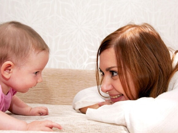 Maman est accroupie face à bébé qui rampe et sourit en le regardant
