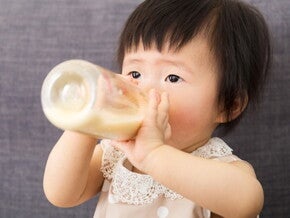 Bébé assis sur un sofa buvant son biberon à deux mains Bébé assis sur un sofa buvant son biberon à deux mains