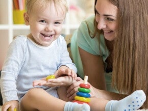 Maman est accroupi à côté de bébé qui joue assis et rigole avec lui Maman est accroupi à côté de bébé qui joue assis et rigole avec lui