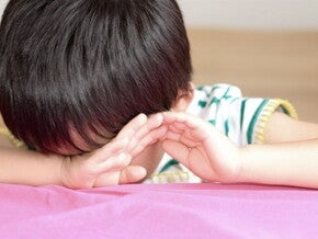 Petit garçon est assis à table la tête cachée dans ses bras et semble bouder Petit garçon est assis à table la tête cachée dans ses bras et semble bouder