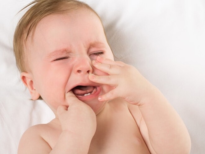 Bébé est allongé sur le dos les mains devant sa bouche et pleure fortement