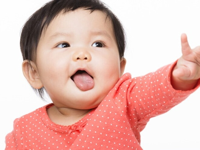 Bébé assis avec un pull rose lève le bras gauche et bouge ses doigts